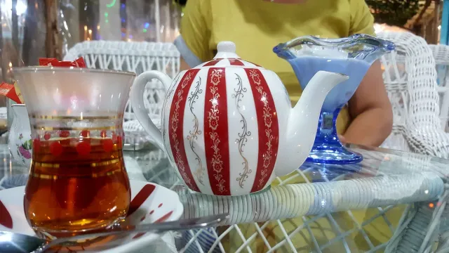 A striped teapot and a glass of tea on a white wicker table