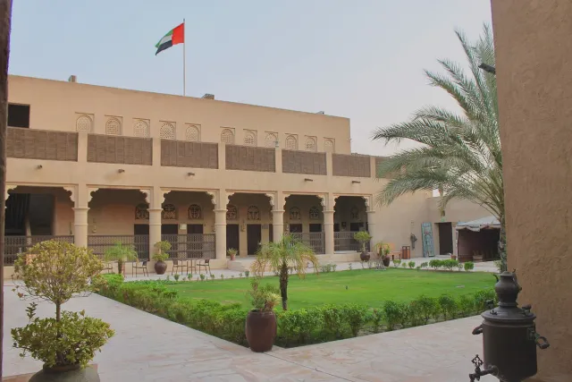 An inner courtyard with a lawn, a row of arched columns and a flying flag