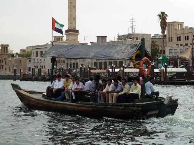 A wooden boat full of passengers crossing a creek in front of the old town