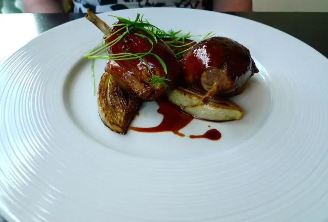 A carefully plated dish on a white plate with dark sauce and herbs
